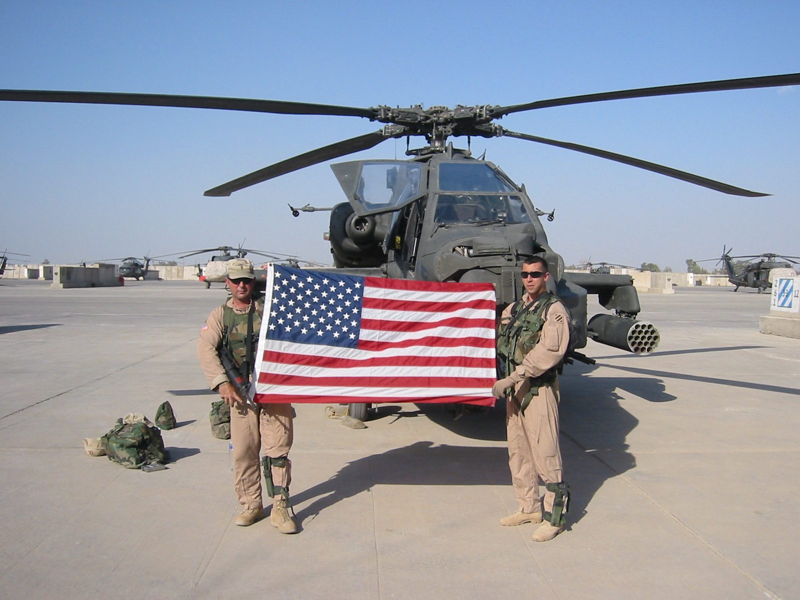 Brian with fellow soldiers and an American flag in front of an Apache helicopter